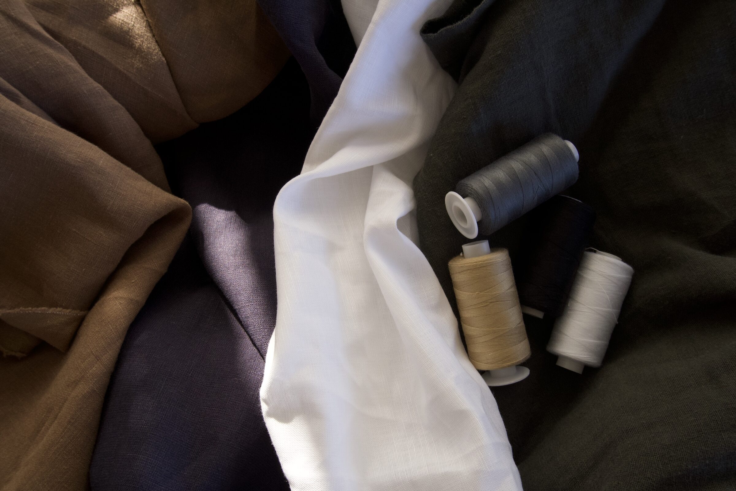 casalino linen blend fabrics in camel, white, charcoal and olive with thread spools